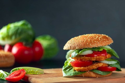 Burger with schnitzel, tomatoes, onions and lettuce on a wooden board, ingredients in the