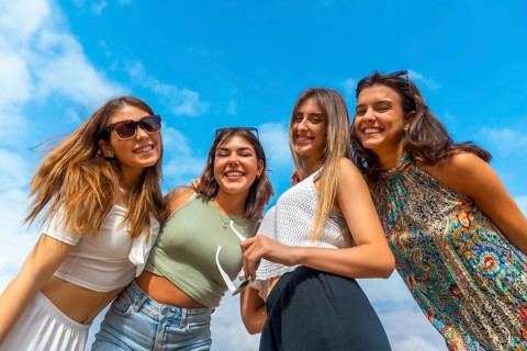 Group of young women standing close together outdoors, smiling and laughing on a sunny summer day