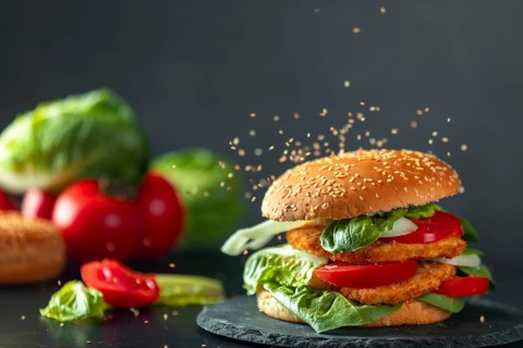 Sesame falls on burgers with schnitzel, tomatoes, onions and lettuce, ingredients in the background