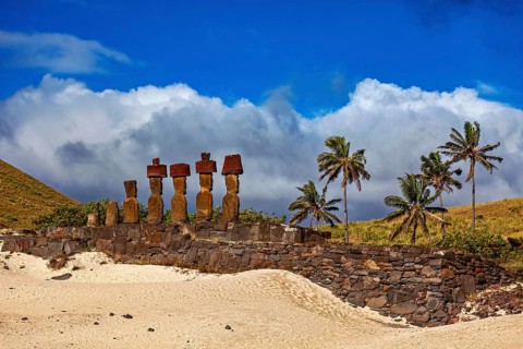 Historic image of stone statues and palm trees, with clouds and blue sky on Easter Island, The Moai