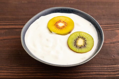 Yogurt, with kiwi in blue bowl on brown wooden background, side view, close up, minimalism