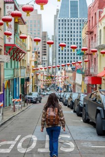 Young person with a backpack walking up a vibrant san francisco chinatown street adorned with
