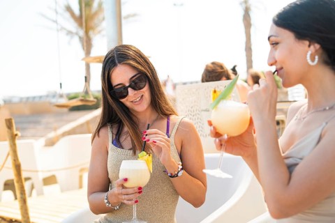 Two friends enjoy refreshing cocktails at a seaside venue. The scene captures a joyful moment of