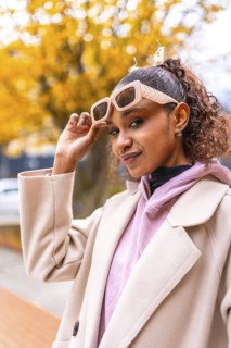 Cool african american woman holding sunglasses to look at the camera wearing coat in the city in