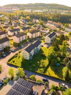 Aerial view of a residential area with forests in the background, many roofs and green areas in