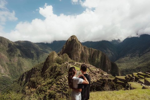 A couple stands atop a hill in Peru, gazing at the majestic ruins of Machu Picchu surrounded by