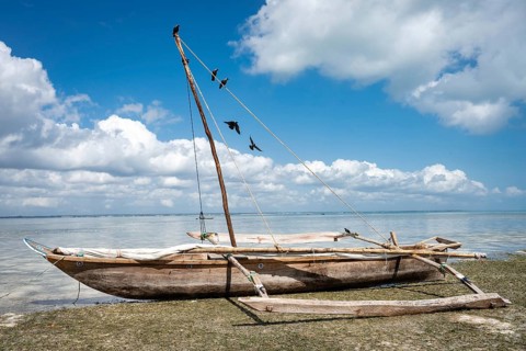 A classic Zanzibar outrigger boat dhow standing on the shore during low tide, reflecting the rich
