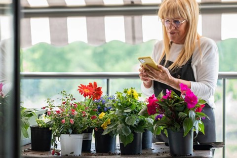 A woman stands on her balcony tending to vibrant potted flowers, capturing the moment on her
