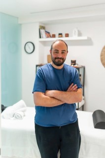 Professional male masseur standing with crossed arms, smiling at the camera in a modern, serene spa