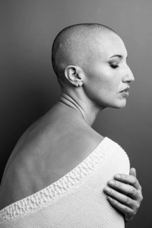 Black and white portrait of a middle aged woman with a shaved head, facing sideways. She wears a