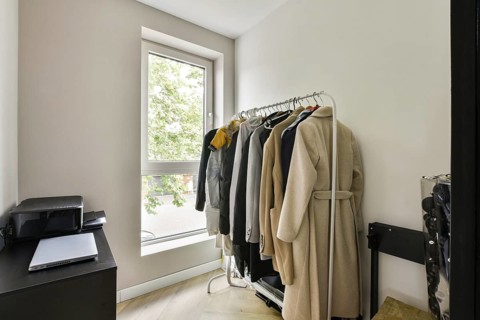 A clean, minimalist interior featuring a clothing rack laden with various garments next to a