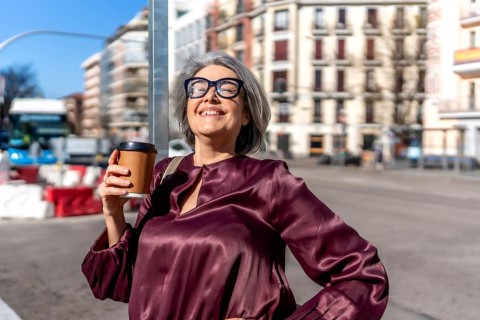 Mature woman with gray hair and eyeglasses smiling, feeling warm sunlight on her face while holding