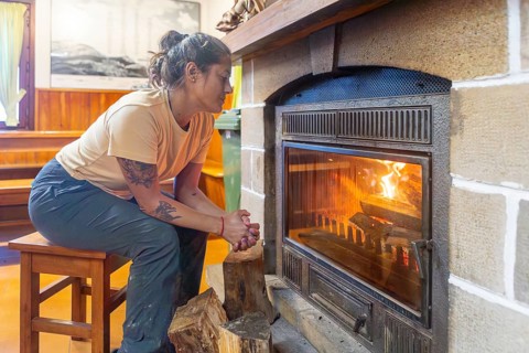 A woman warms herself by a cozy fireplace in a rustic shelter in Gorbea Natural Park, Basque