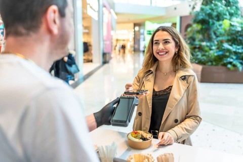Young woman smiling as she makes a contactless mobile payment for a meal at a bustling shopping