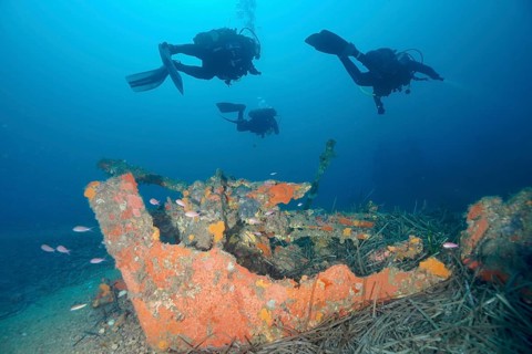 Three divers explore a colorful ship fragment on the seabed, Wreck Michel C dive site, Giens