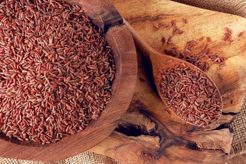 Natural, red rice, in a wooden bowl and spoon on a wooden surface in rustic style, top view