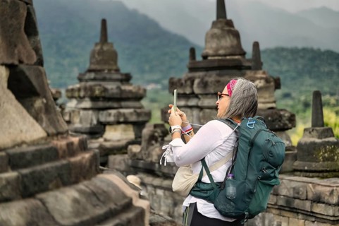 Side view of a female senior tourist capturing photos with a smartphone at the historic Borobudur