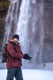 A photographer taking pictures in winter at the Seljalandsfoss waterfall with snow in Iceland