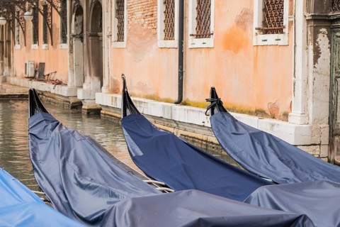 Covered gondolas float serenely beside a historic Venetian building, showcasing the unique beauty