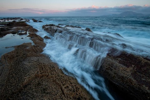 The rocky coast of Tarifa, Cadiz, during sunset. Waves gently cascade over rocks, capturing the