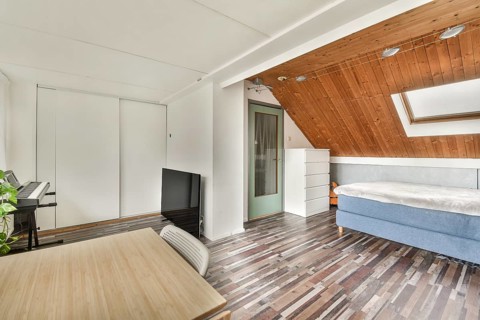 A bright attic bedroom featuring a wooden ceiling, skylight, and contemporary decor. Includes a