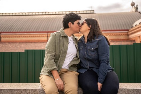 A curvy lesbian couple in casual attire shares a heartfelt kiss outdoors, symbolizing love and