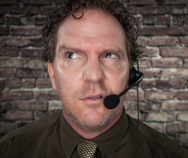 Unfriendly Confused Businessman with Frowning Face Wearing Phone Headset In Office with Brick
