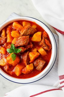 Potatoes stewed with meat, in tomato sauce, with spices and herbs, no people, on a white table