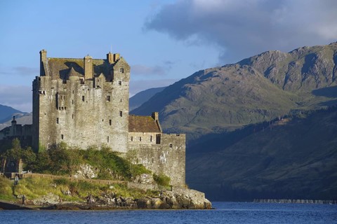 A majestic waterfront castle with mountains in the background under a dramatic sky, film set,