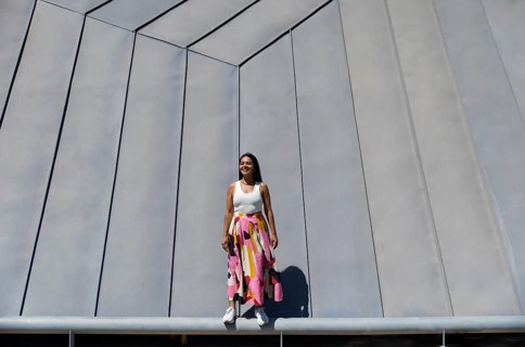 A woman in a vibrant, colorful skirt stands confidently in front of a striking piece of modern