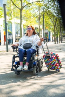 Smiling redhead tourist enjoying summer vacations, riding her electric wheelchair and pulling