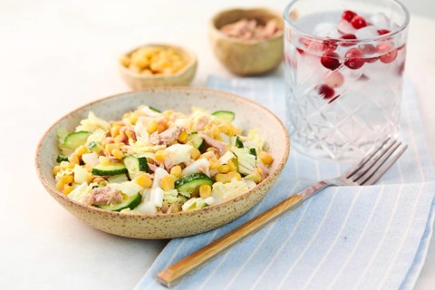 A fresh tuna salad with cucumbers and corn served in a bowl. Accompanied by a refreshing glass of