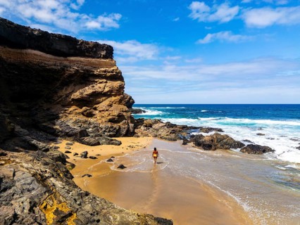 From above a lone woman walks on the sandy shore of Tindaya Beach in Fuerteventura, amidst rugged