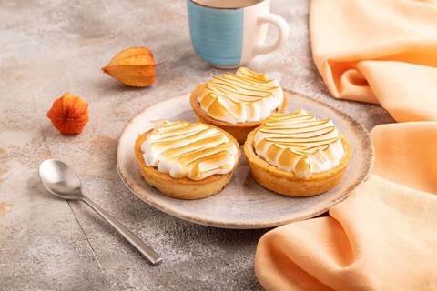 French lemon tart with meringue on brown concrete background, cup of coffee, orange linen textile,