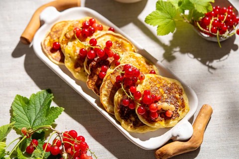 Top view of fluffy pancakes topped with vibrant red currants, elegantly arranged on a white ceramic