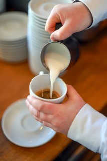 Germany - Barista prepares a coffee, here a cappuccino, hand pours milk foam from a pot into a cup