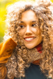 Vertical close-up portrait of a sensual beauty woman with curly hair looking away in a park in