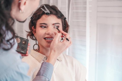 Professional makeup artist applying eyeshadow on a smiling model in a bright makeup studio,