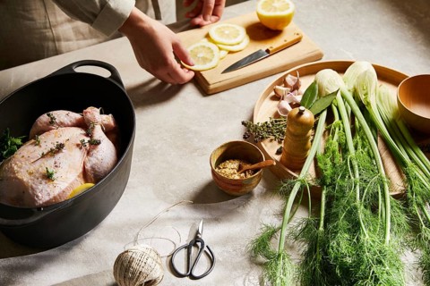A butcher prepares a savory chicken dish with fresh ingredients, including lemon slices and fennel,