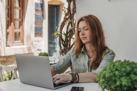 A focused woman working on her laptop outdoors. She appears engaged and concentrated, highlighting