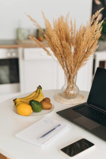 A clean workspace featuring a laptop, open notebook, and a plate of fresh fruits including bananas,