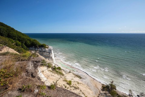 White chalk cliffs in August. People on the beach and by a small lagoon. Milky Baltic Sea under a