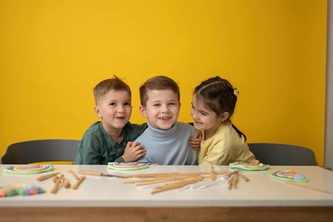 Three smiling children engage in a creative play lesson, surrounded by colorful clay and tools on a