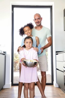 A joyful father with his two daughters enjoying a day at home. The younger child holds a bowl of