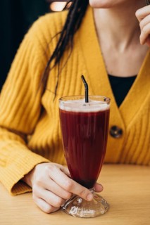 A woman in a yellow sweater holds a tall glass with a refreshing coffee and a straw She sits at a