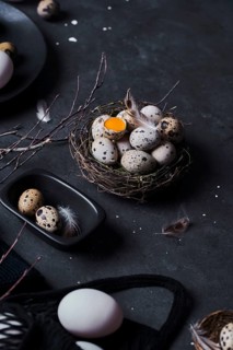 From above composition of raw chicken eggs on plates and quail eggs in nest on black background