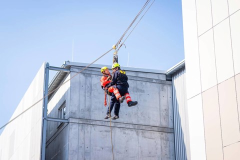 Two rescue workers in protective suits hang from a rope on the side of a building, Hospital