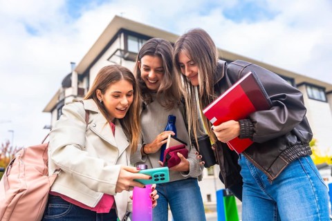 Young women college students checking social media content on a smartphone, sharing a moment and