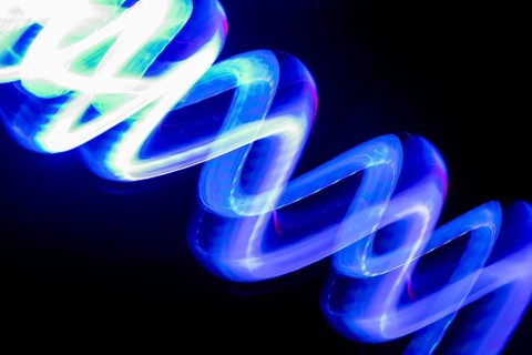 Vibrant blue neon light trails create dynamic patterns on a dark background. This long-exposure