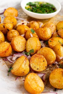 Roasted potatoes sit on a baking sheet next to chopped herbs and red onions. They are golden brown